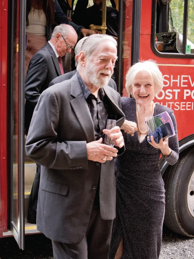 An older man and woman step off of an older red bus